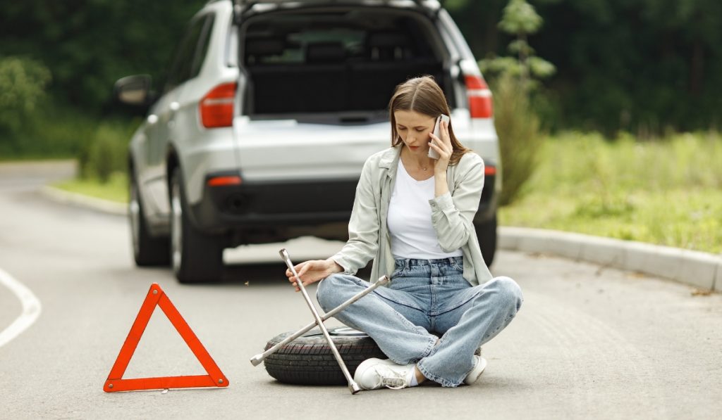 Car breakdown leads to a flat tire needing towing assistance on a quiet road surrounded by greenery