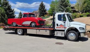 Vehicle towing service in Fort Collins transports classic red truck on flatbed during sunny day